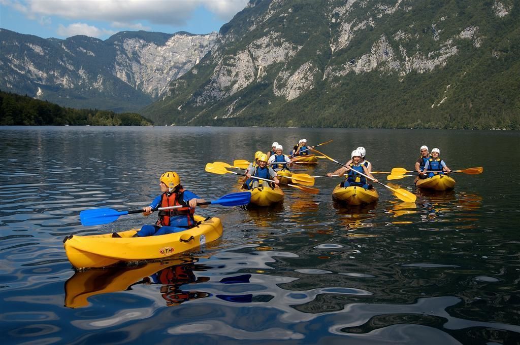 Un groupe de personnes fait du kayak sur un lac paisible, avec des montagnes en arrière-plan.