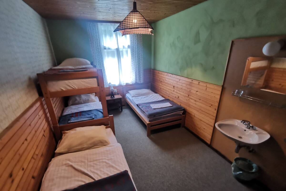 A small, cozy room with bunk beds, a single bed, a wooden dresser, a mirror, and a sink.