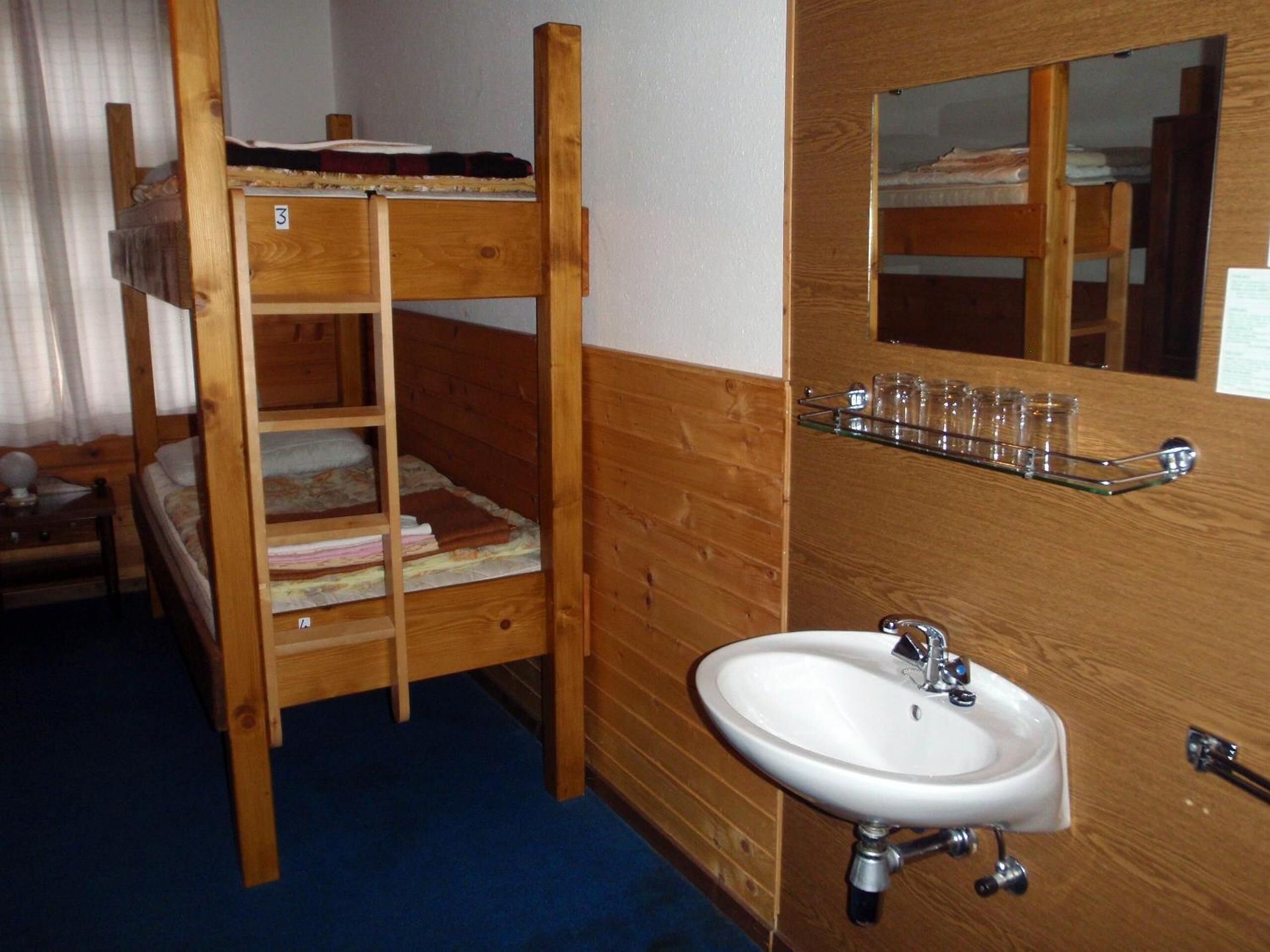 A bunk bed with a shelf above it, a wooden wall, a sink, and a mirror.