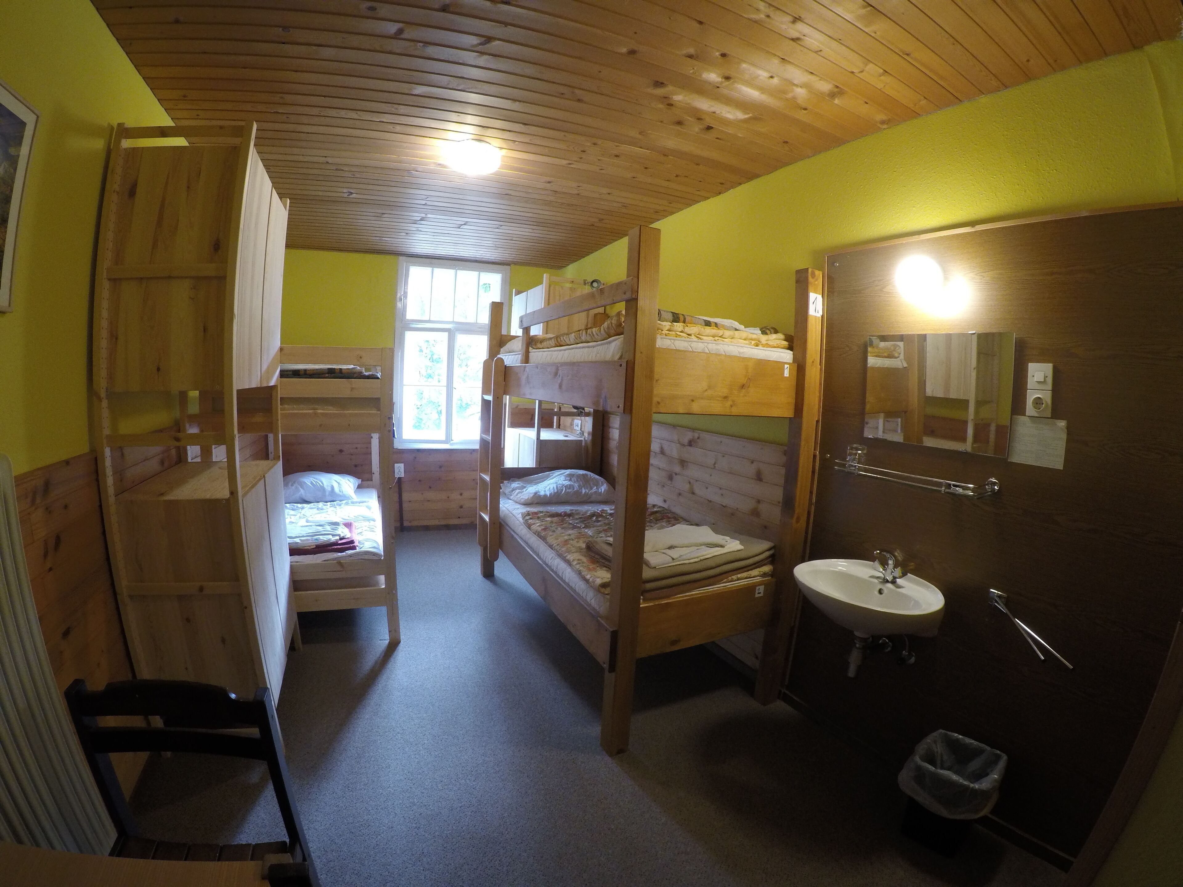 Een slaapzaal met stapelbedden, een houten plafond, een raam, een wastafel en een spiegel.