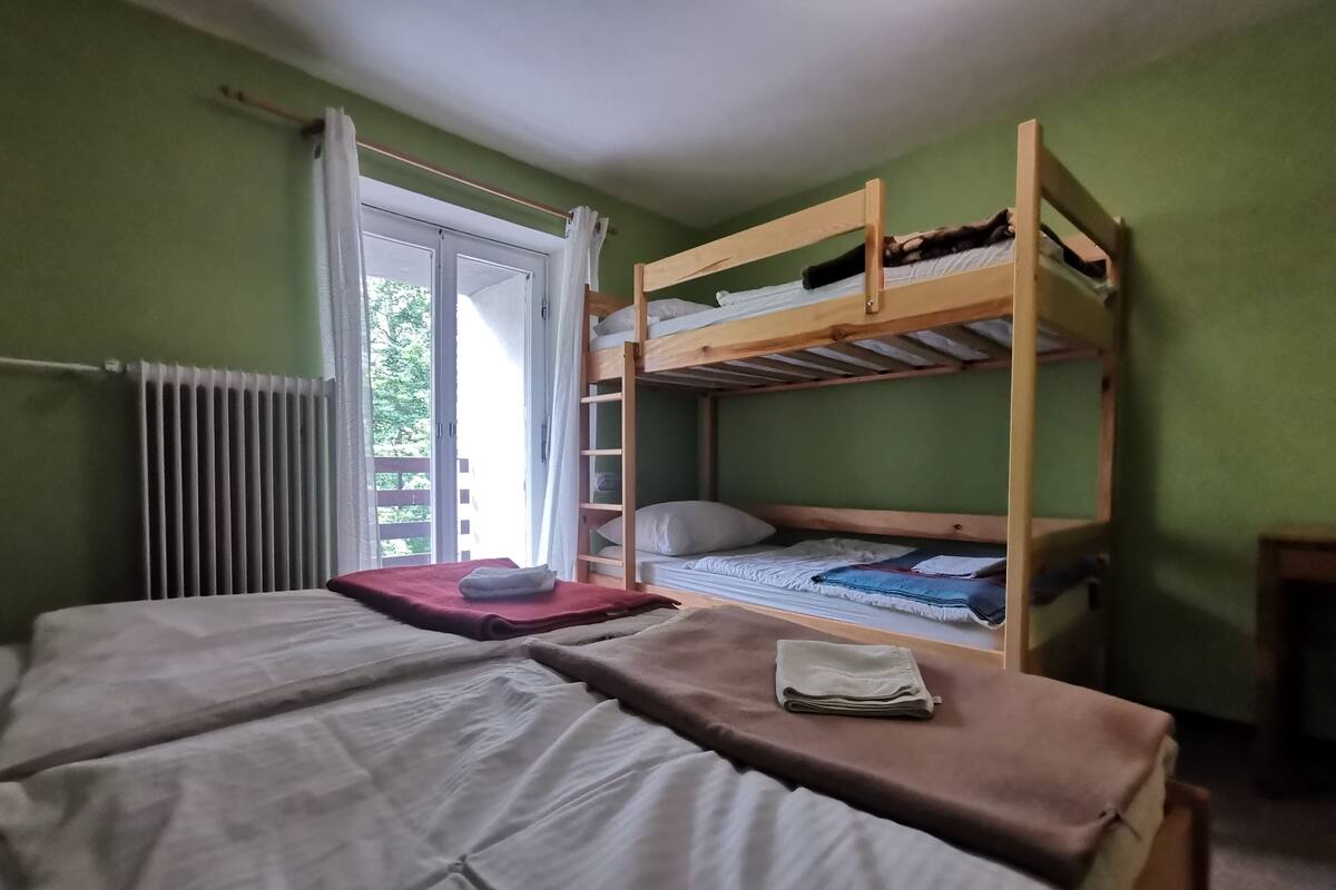 A bunk bed room with a window, a radiator, and a neatly made bed.