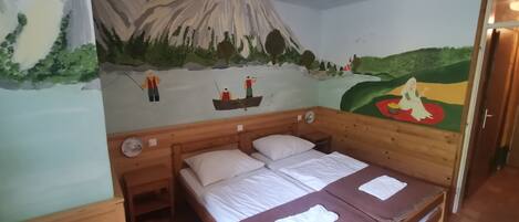 A room with a bed, a wooden headboard, a nightstand, and a wall mural depicting a mountain scene with people fishing.