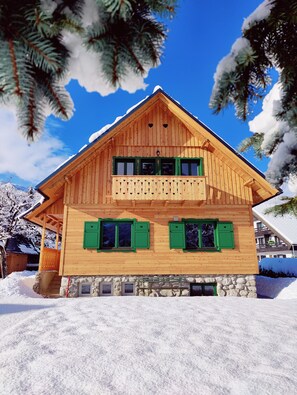 A wooden chalet with a stone foundation, green shutters, and a balcony with heart-shaped cutouts. - Cottage Suha (Bohinj)