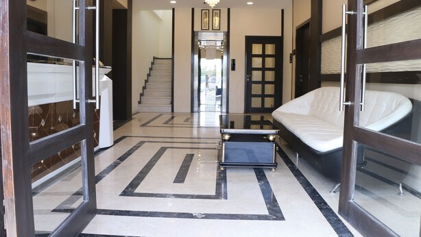 Un hall d’hôtel au design moderne, avec un escalier central, un coin salon comprenant un canapé et une petite table, ainsi qu’un grand miroir qui reflète l’espace.