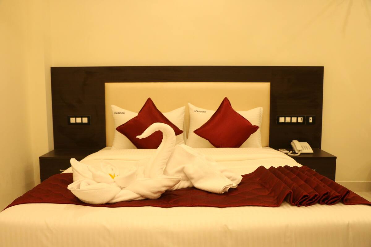 A neatly made bed with a red and white color scheme, a headboard, and a bedside table with a phone.