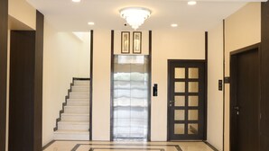 Un hall d’entrée moderne avec un sol en marbre, un escalier, un ascenseur et une porte dotée d’un panneau en verre.
