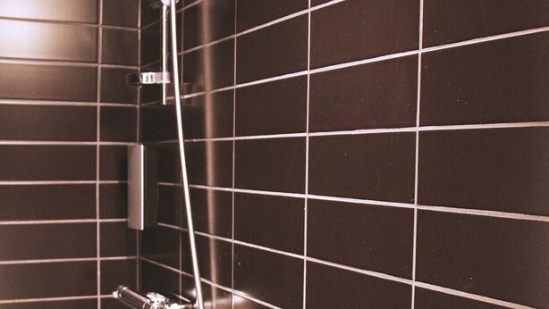 A bathroom with dark tiled walls and a shower with a handheld showerhead and a handheld faucet. - Hotell Västmannagatan no.61 (Stockholm)
