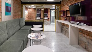 Un vestíbulo moderno con pared de ladrillo, un sofá gris y una recepción con televisor.