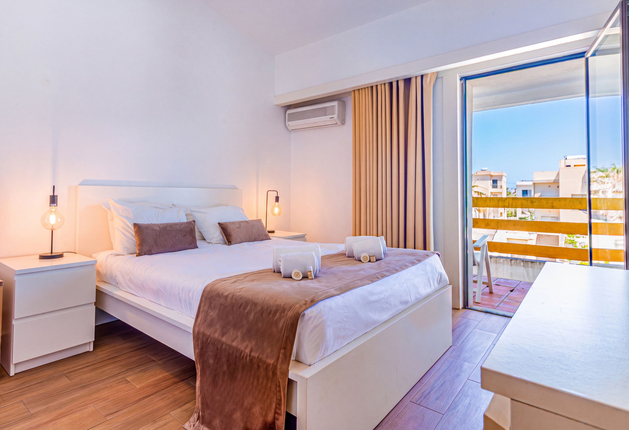 A hotel room with a bed, bedside tables, a lamp, a towel, and a view of the outside.