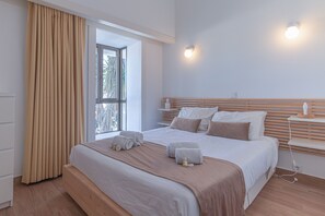 Quarto moderno com uma cama grande, mesa de cabeceira, janela com cortinas e luminária fixada na parede.