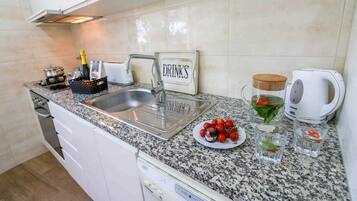 A kitchen with a granite countertop, stainless steel sink, a toaster, a kettle, and a sign that says 'DRINKS'.