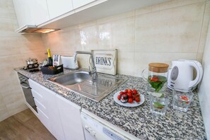 Una cocina con encimera de granito, pileta de acero inoxidable, tostadora, hervidor y un cartel que dice 'DRINKS'.