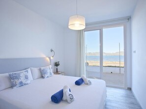 Un dormitorio con una cama grande, una mesita de noche, una lámpara y vista al mar.