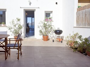 Un patio con mesa y sillas, una parrilla, plantas en macetas y vistas a través de una puerta abierta.