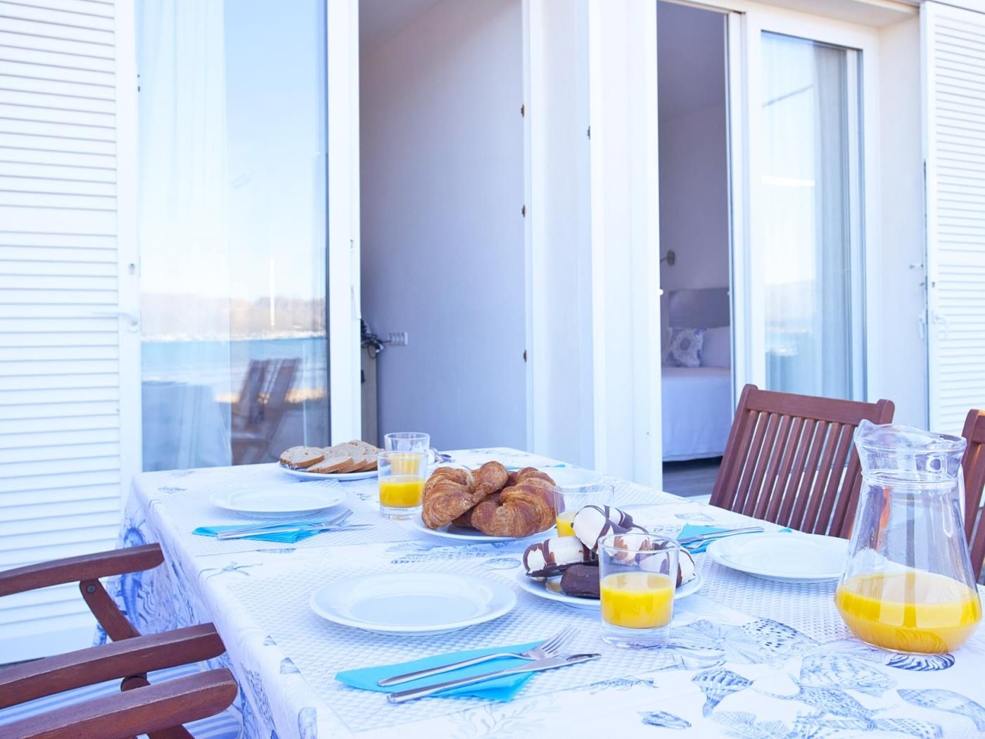 A breakfast table set on a balcony with a view, featuring croissants, orange juice, and a bottle of juice.