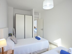 Ein Hotelzimmer mit zwei Betten, einem Kleiderschrank, einem Schreibtisch mit Lampe und Blick auf den Flur.