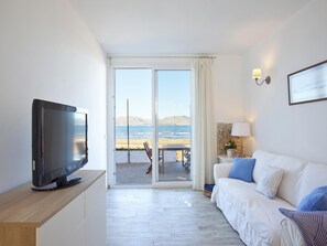 A modern hotel room with a flat-screen TV, a sofa, a table, and a view of the sea through a glass door. - Ran de mar · A modern and comfortable beachfront house in Alcudia (Alcúdia)