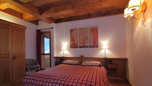 Un dormitorio con una cama de madera, dos mesitas de noche con lámparas, un armario de madera y un ventanal con cortinas.