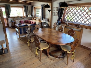 A wooden dining table with chairs, a sofa, and a window with curtains. - Holiday chalet in Borca di Cadore - Dolomites - 15 km to Cortina d'Ampezzo# (Borca di Cadore)