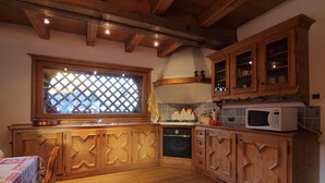 Una cocina con armarios de madera, un ventanal con celosía y un microondas en la encimera.