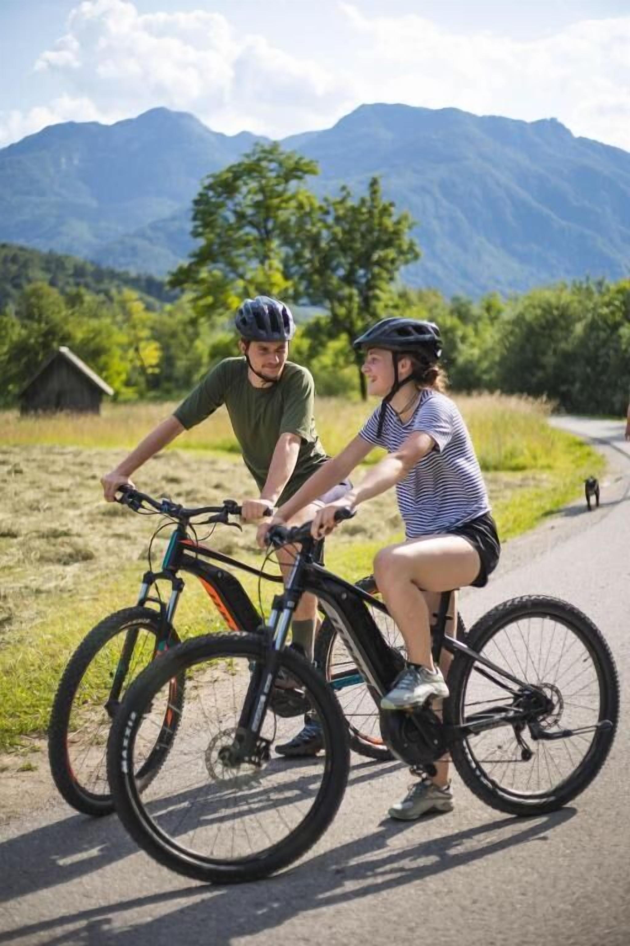 Två personer på cyklar på en asfalterad stig med ett berg i bakgrunden.