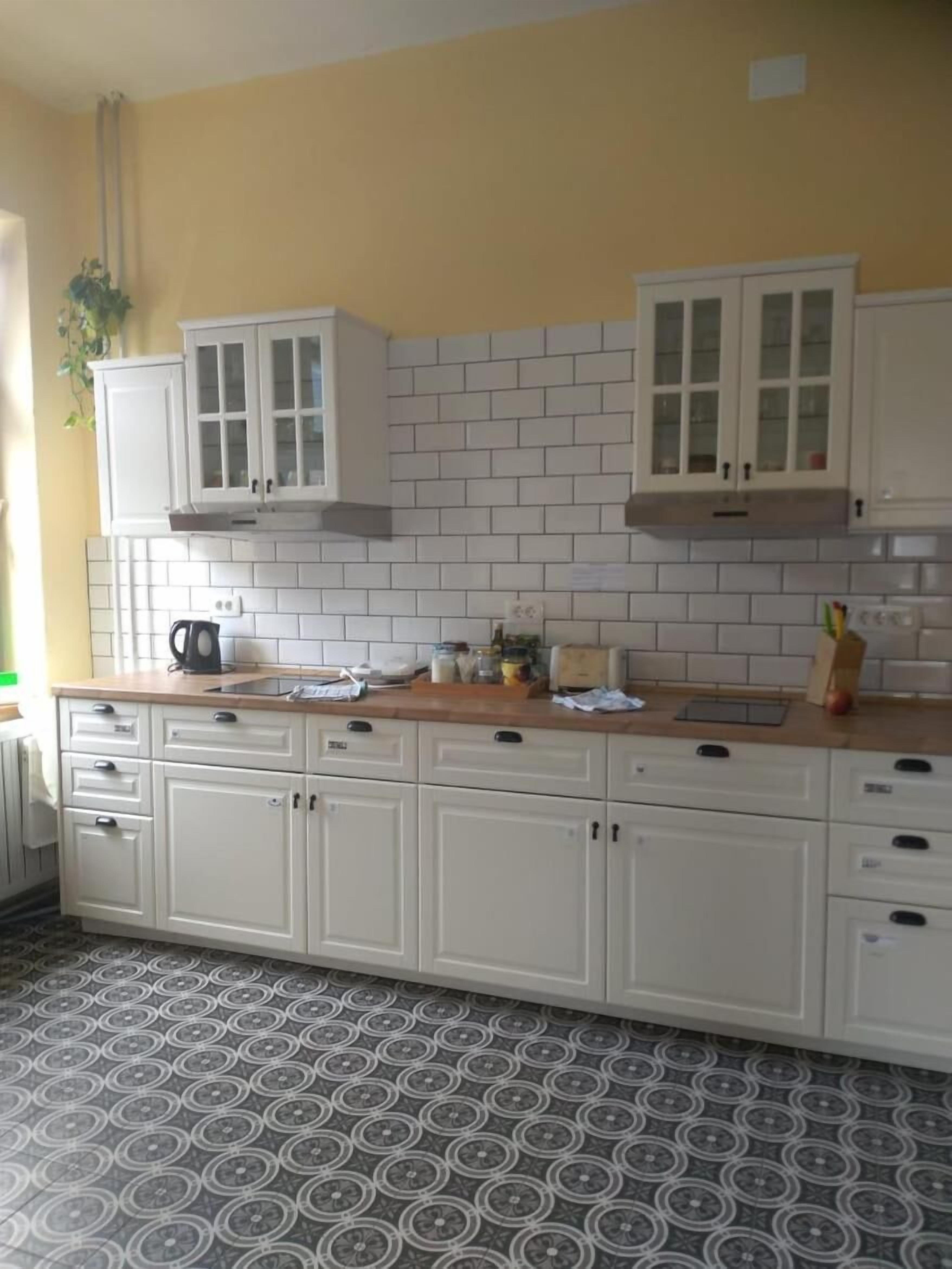 Una cocina con armarios blancos, salpicadero de azulejos y suelo estampado.