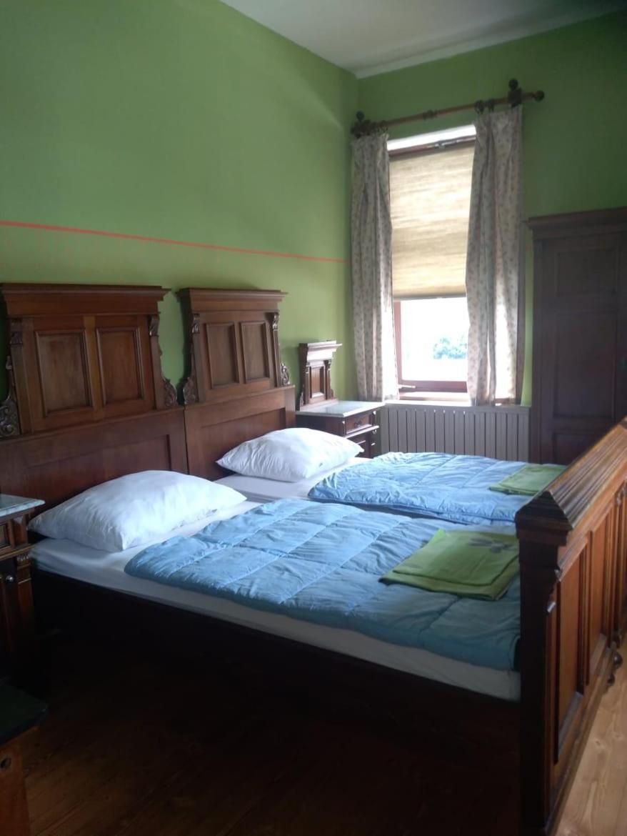 Une chambre avec deux lits, des têtes de lit en bois, une fenêtre avec des rideaux et un radiateur.