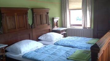 Une chambre avec deux lits, des têtes de lit en bois, une fenêtre avec des rideaux et un radiateur.