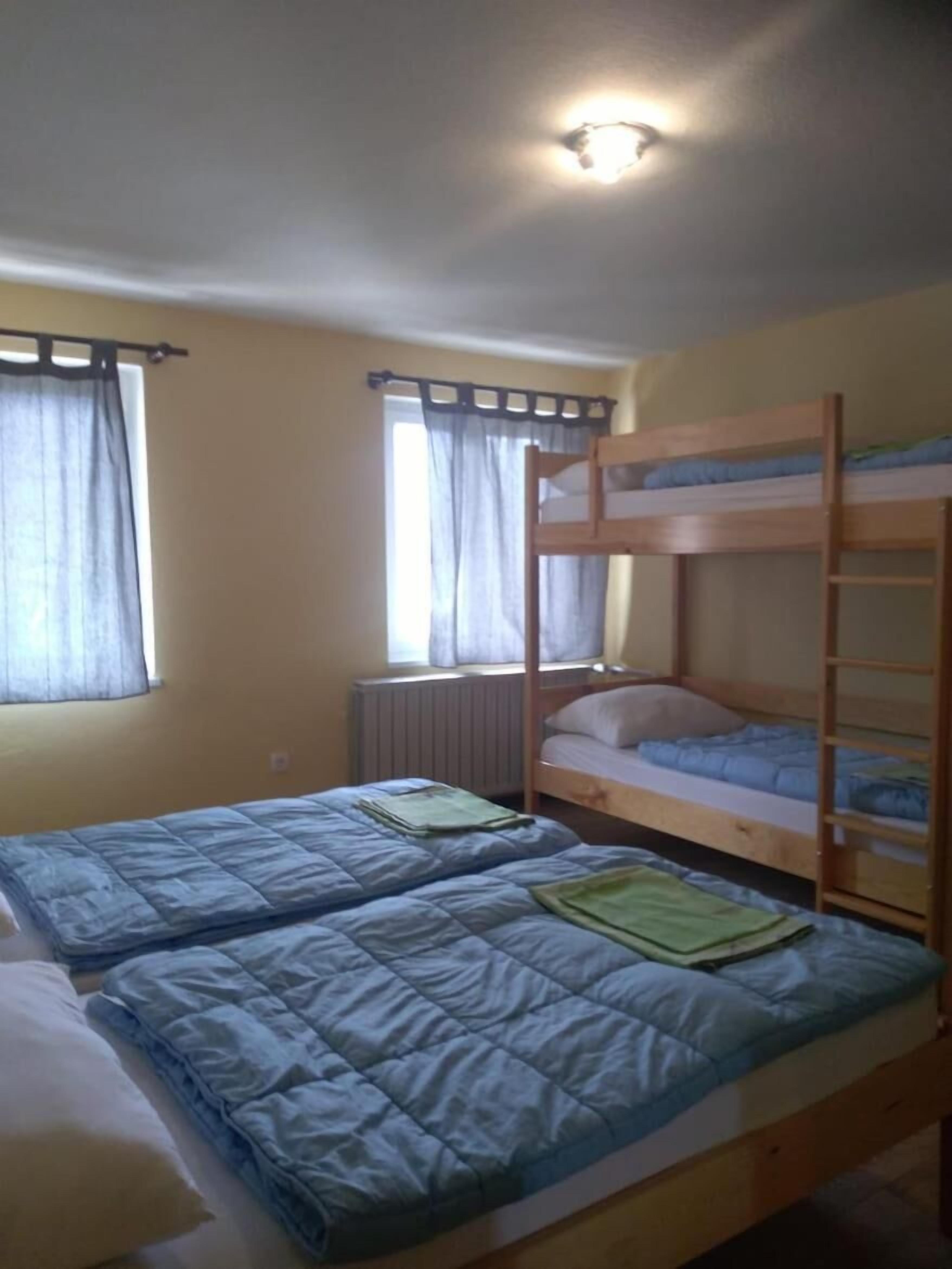 A dormitory room with two bunk beds, a radiator, and a window with curtains.