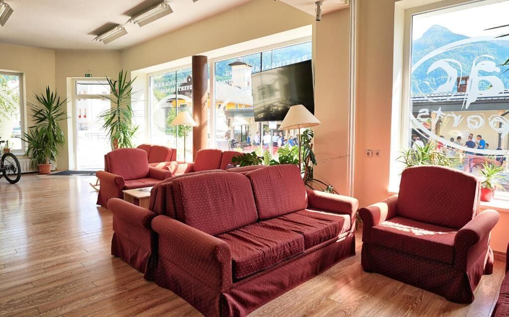 A spacious living area with a red sofa set, a television, and large windows offering a view of the outside.
