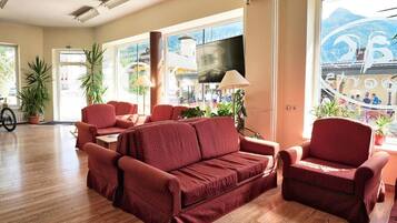 A spacious living area with a red sofa set, a television, and large windows offering a view of the outside.