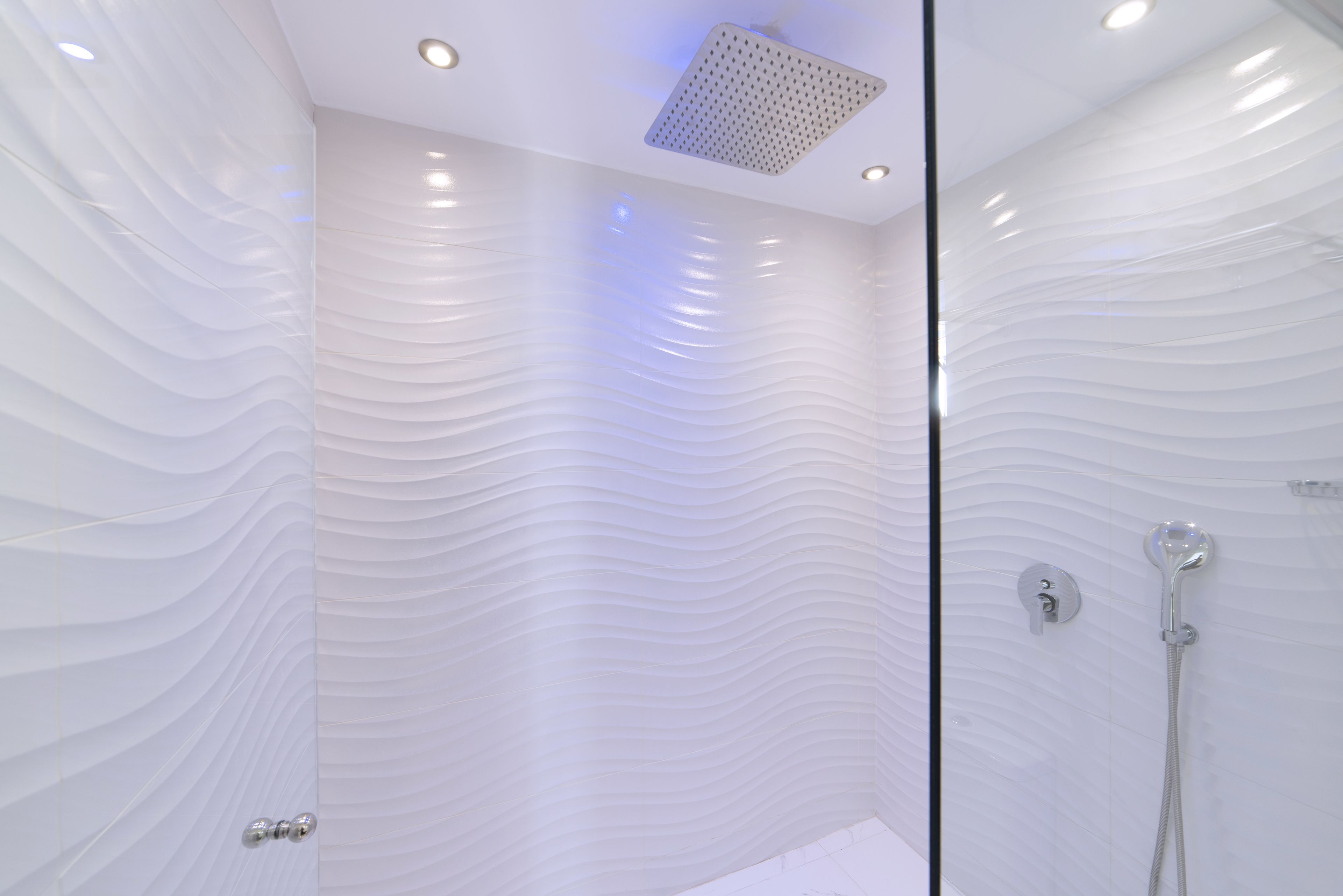 Ein modernes Badezimmer mit einer wellenförmigen Wandgestaltung, einer Duschbrause und einer Glasabtrennung.