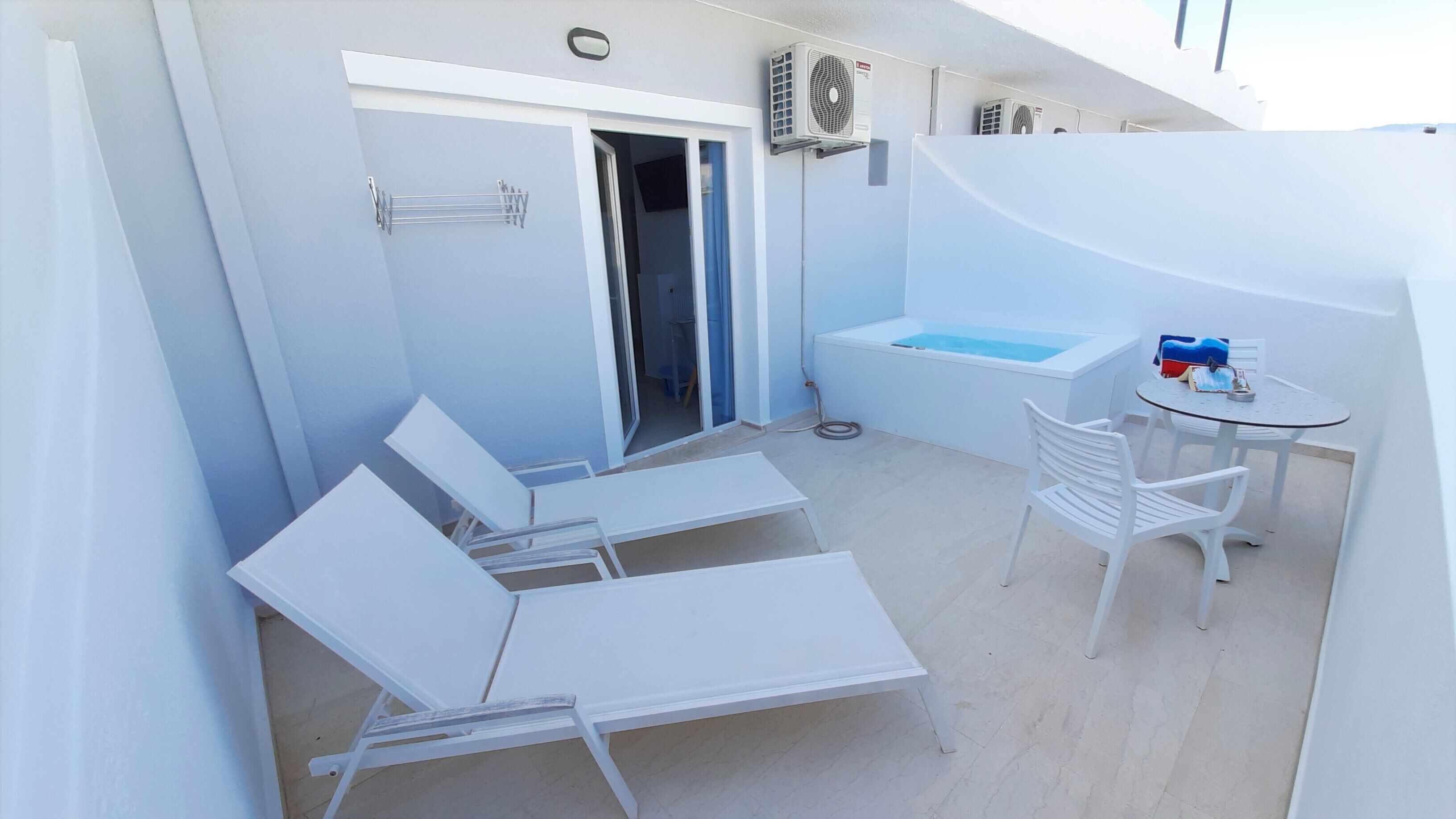 Un balcon avec deux fauteuils de relaxation blancs, une petite table avec une bouteille et un jacuzzi intégré.