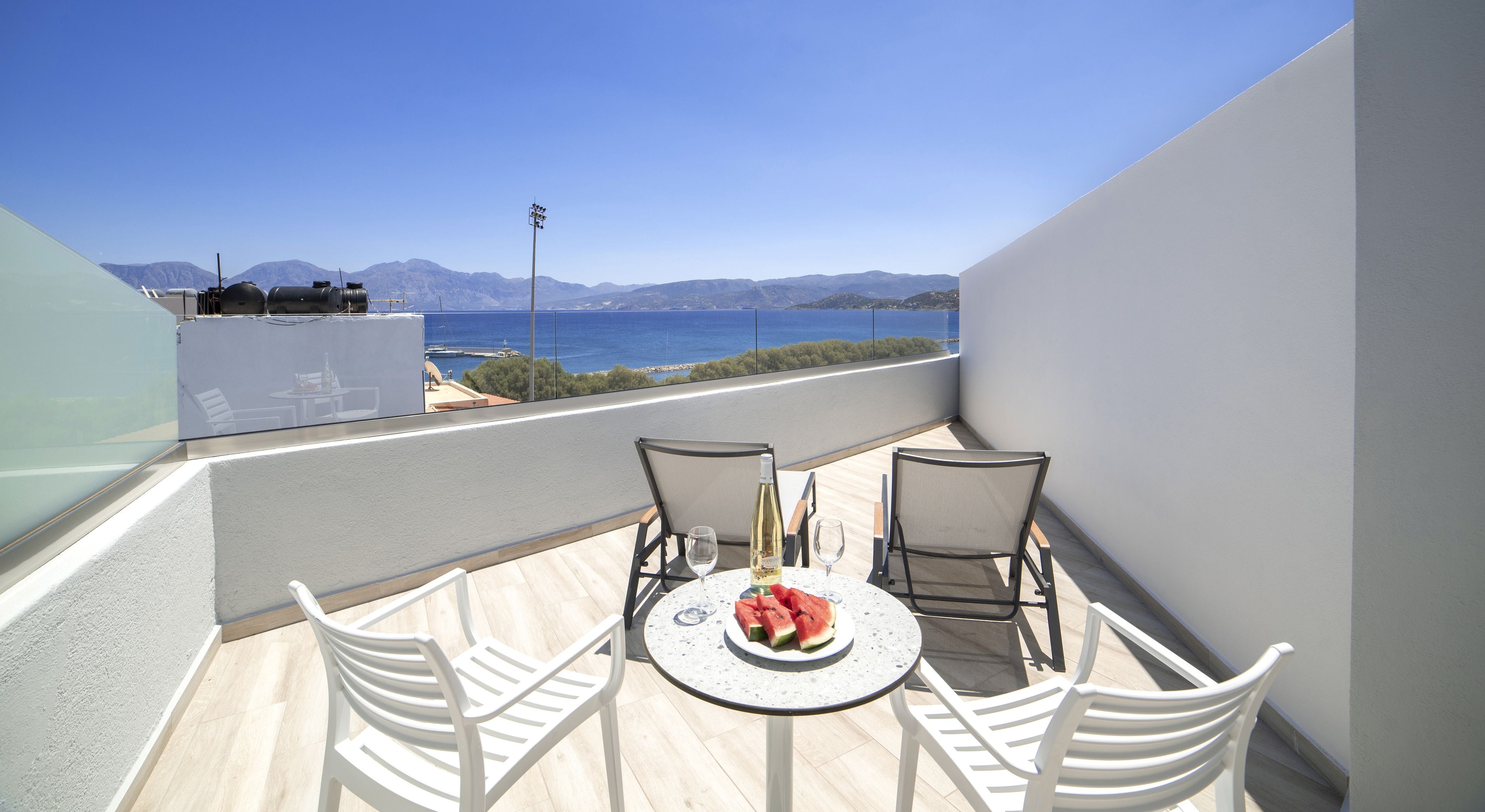A balcony with a table and chairs, a bottle of wine, and a plate of watermelon.