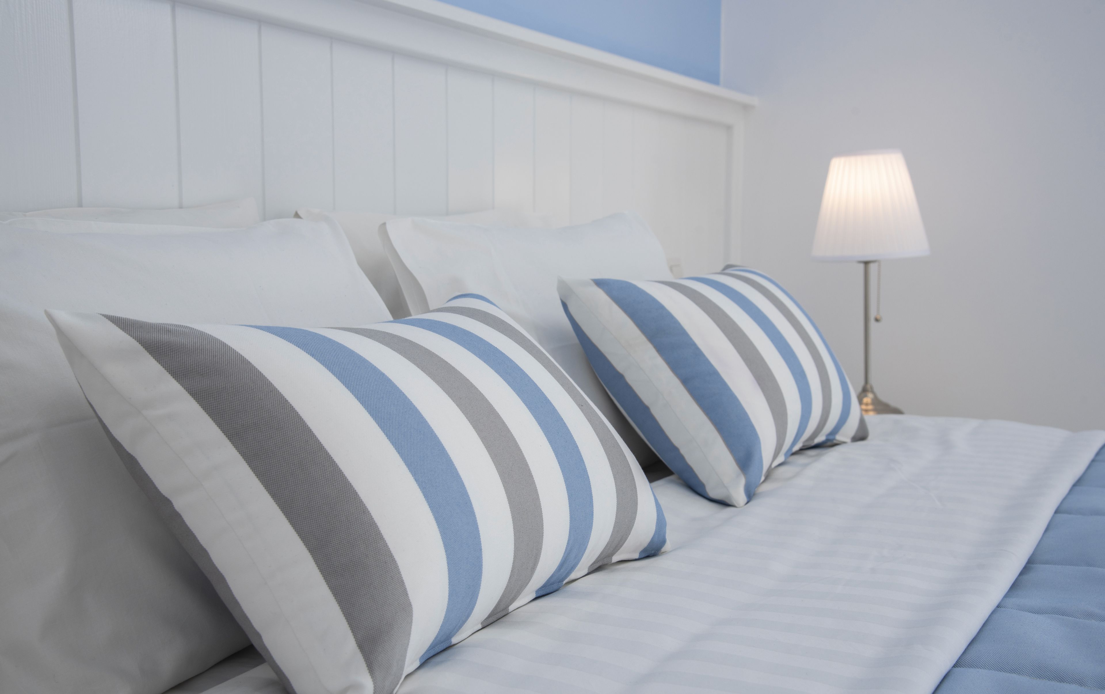Cama bem arrumada com almofadas listradas e abajur.