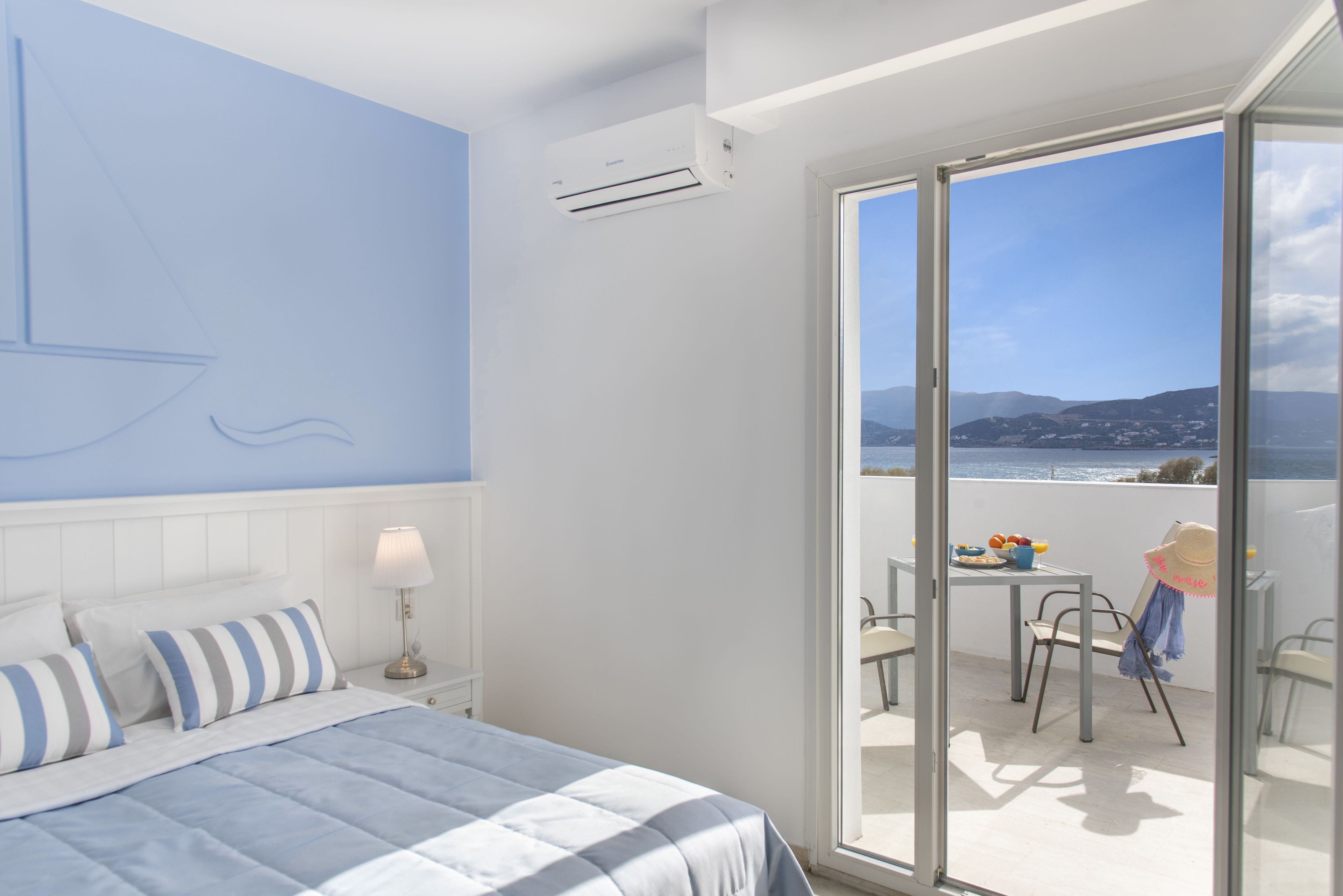 A bedroom with a bed, a nightstand, a lamp, and a view of a balcony with a table and chairs.