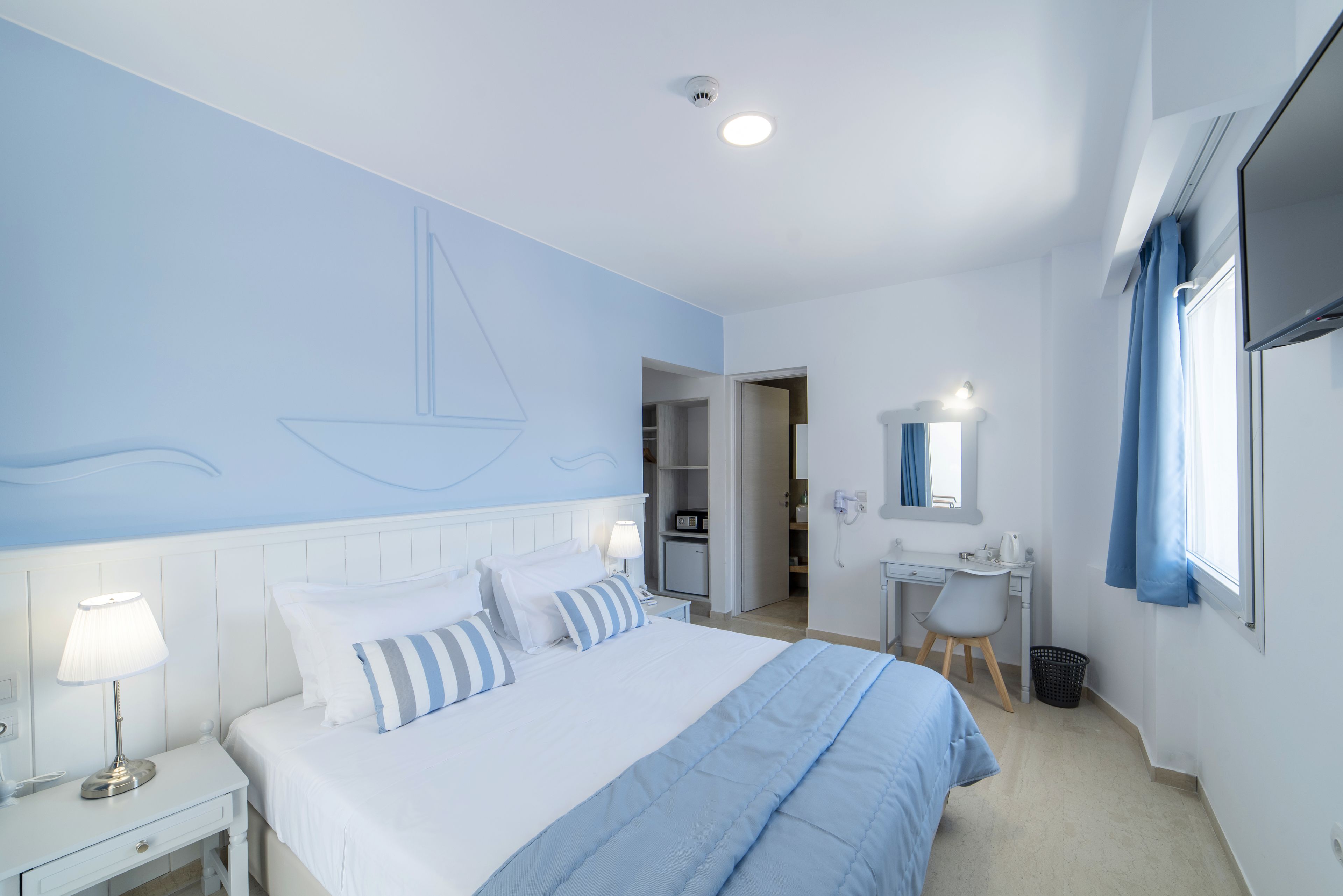 A bedroom with a bed, bedside table, lamp, and a desk with a chair.