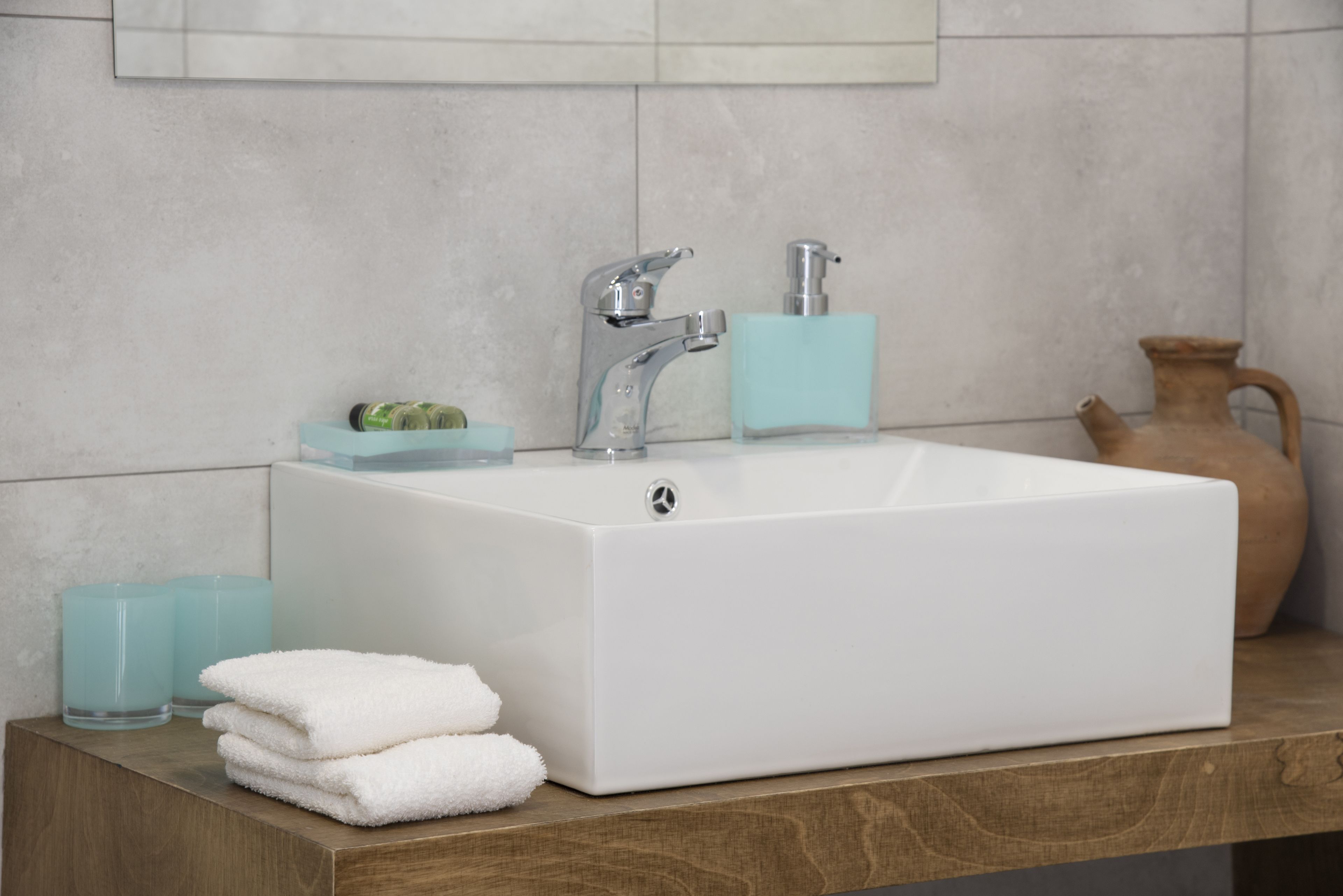 Un baño con un lavabo blanco, dos grifos, un dispensador de jabón y una jarra en la encimera.