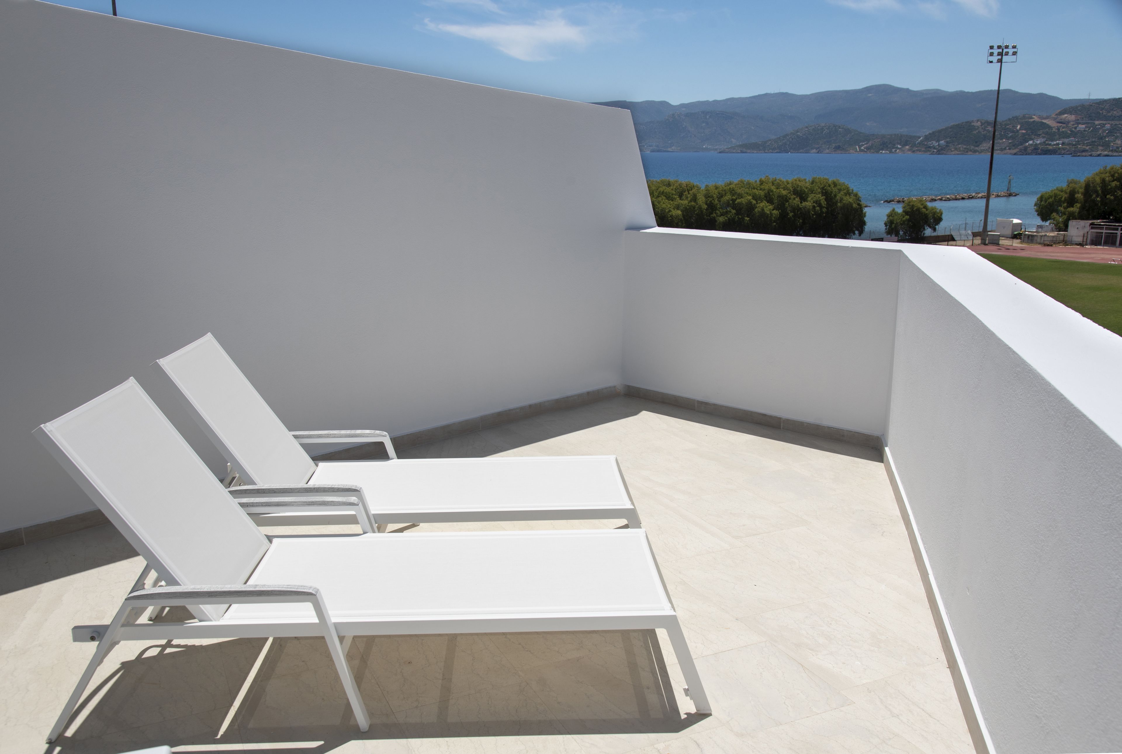 Un balcon avec des fauteuils de jardin blancs, une vue sur la mer et un paysage montagneux en arrière-plan.