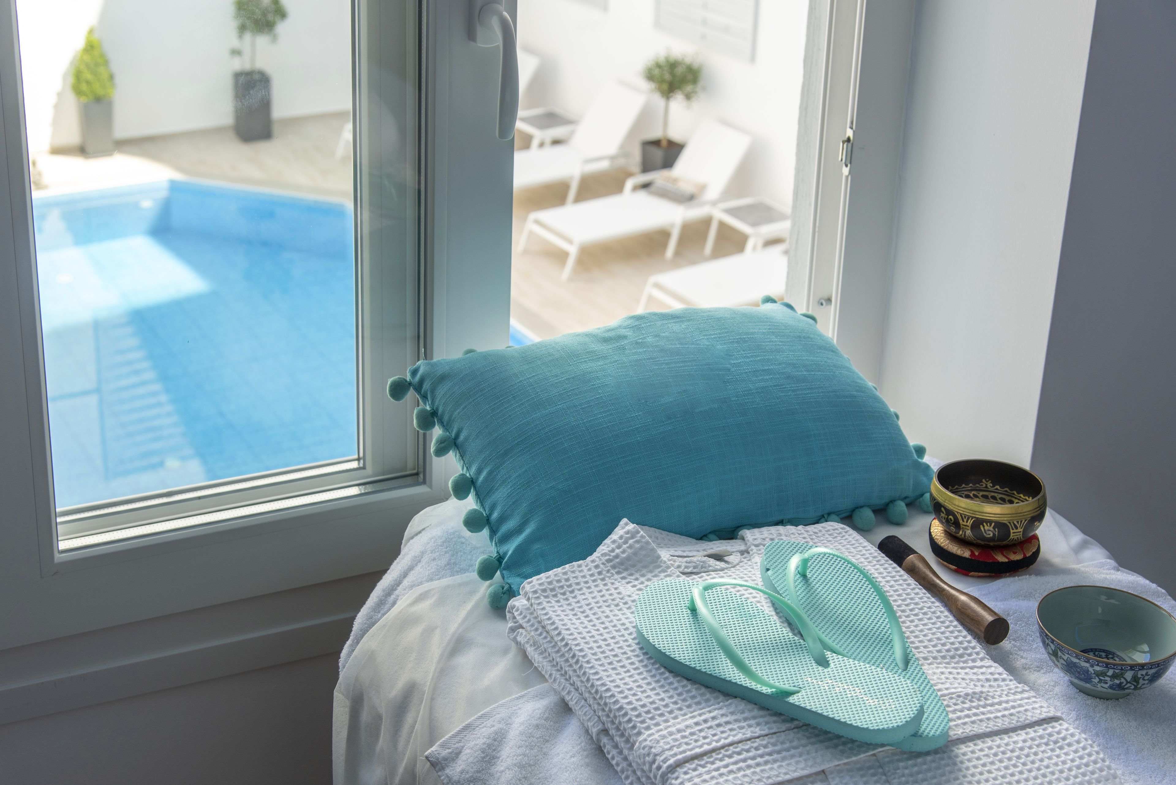 Een bed met uitzicht op een zwembad, een raam en een klein tafeltje met een kom en een boek.