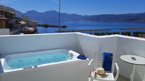 A rooftop terrace with a hot tub, a chair, a table, and a view of the sea and mountains. - Naiades Marina Hotel (Agios Nikolaos)