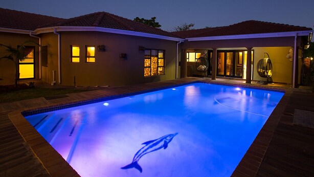 Una piscina con diseño de delfín, rodeada por una casa de techo con tejas y múltiples ventanas.