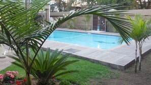A rectangular swimming pool with a wooden deck surrounding it, set in a landscaped garden with various plants and a small grassy area.
