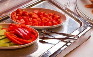 Un plateau en acier inoxydable contenant deux bols de légumes coupés en tranches : un bol de tomates et l’autre de poivrons rouges et de concombres.