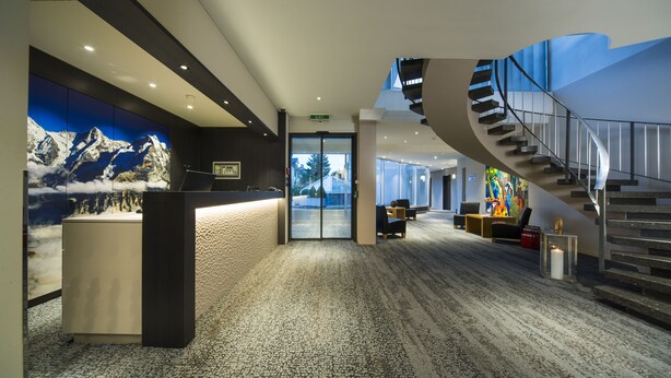 Un hall d’entrée moderne avec un comptoir d’accueil, un escalier en colimaçon et une fresque représentant une montagne.