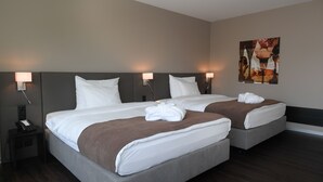 Une chambre d’hôtel avec deux lits, chacun doté de draps blancs et d’une couverture marron, une table de chevet avec un téléphone et des lampes fixées au mur.