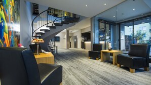 Un hall d’hôtel moderne doté d’un escalier en colimaçon, d’un espace salon, d’un comptoir d’accueil et d’une grande fenêtre offrant une vue sur l’extérieur.