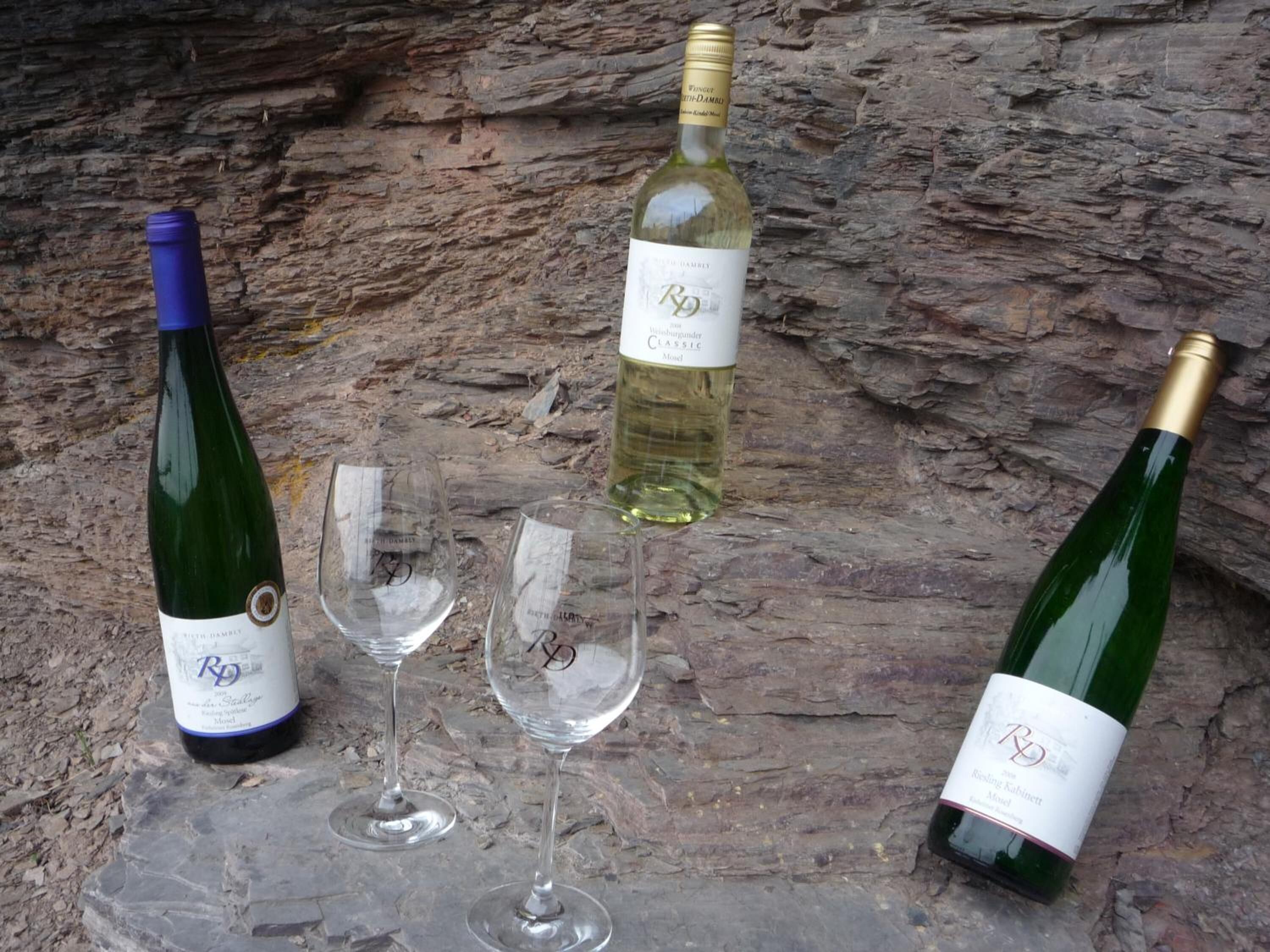 Três garrafas de vinho e duas taças de vinho sobre uma superfície de pedra.