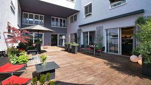 A modern outdoor patio area with wooden flooring, seating arrangements, and potted plants. - Hotel4you (Dorfen)