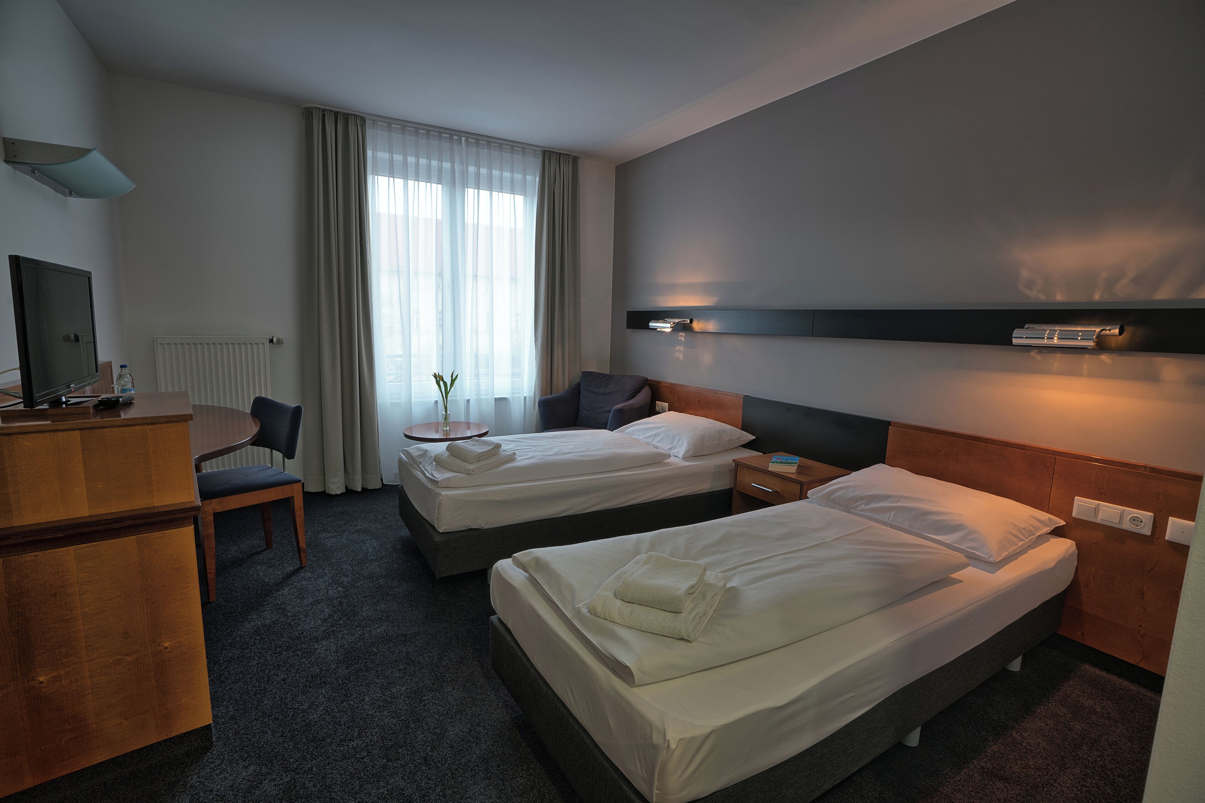 Ett hotellrum med två sängar, ett skrivbord, en stol och en tv.